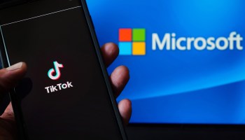 In this photo illustration, a mobile phone featuring the TikTok app is displayed next to the Microsoft logo.
