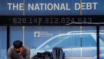 A man waits at a bus stop that displays the national debt of the United States on June 19, 2020 in Washington, D.C.
