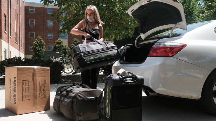 A student wearing a mask at Ohio State University removes luggage from a car on moving-in day in August..