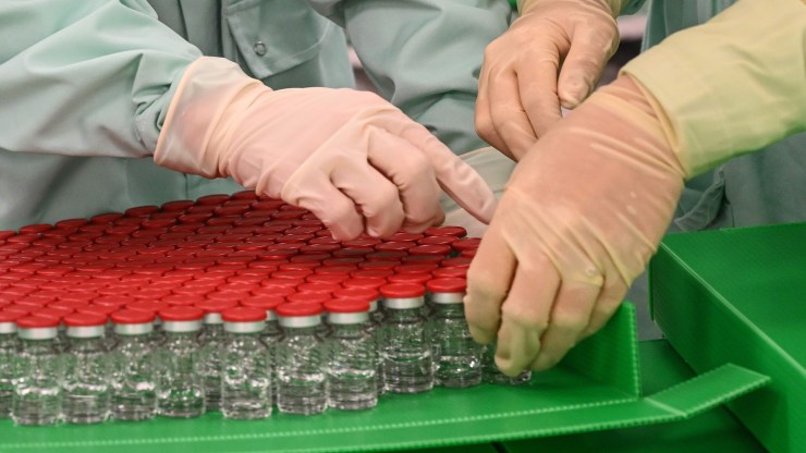Laboratory technicians handle capped vials as part of filling and packaging tests for the large-scale production and supply of the University of Oxford's COVID-19 vaccine candidate, AZD1222, conducted on a high-performance aseptic vial filling line on September 11, 2020 at the Italian biologics manufacturing facility of multinational corporation Catalent in Anagni, southeast of Rome, during the COVID-19 infection, caused by the novel coronavirus.