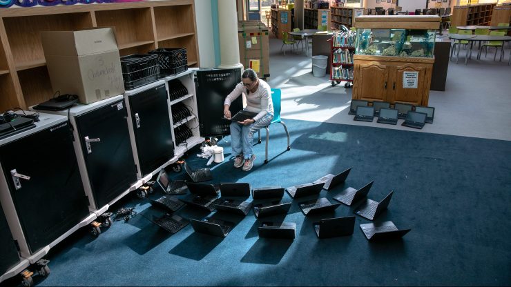 A woman cleans laptops with disinfectant wipes in an elementary school.