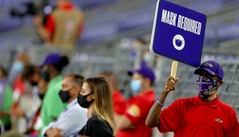 A person walks on the sidelines holding up a sign reading "mask required" during the game between the Baltimore Ravens and Kansas City at M&T Bank Stadium on September 28, 2020 in Baltimore, Maryland.