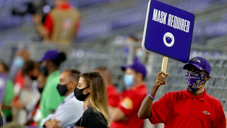 A person walks on the sidelines holding up a sign reading "mask required" during the game between the Baltimore Ravens and Kansas City at M&T Bank Stadium on September 28, 2020 in Baltimore, Maryland.