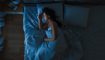 A woman asleep in a bed at night.