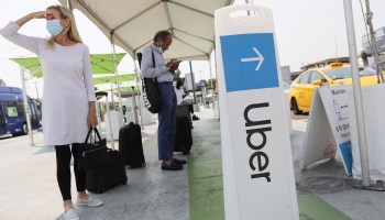 Air travelers wait in the ride-hailing lot near a sign for Uber at Los Angeles International Airport in August.