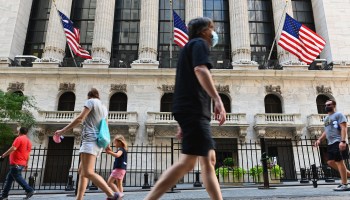 People wearing face masks walk by The New York Stock Exchange in August.