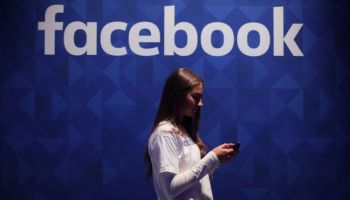 A woman looks at her phone in front of Facebook branding.