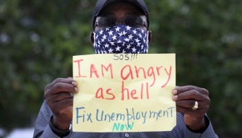 A protester holds a sign calling for a fix to unemployment benefits at a protest in Miami Beach, Florida.