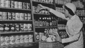 A woman taking canned goods from the shelves of a grocery store circa 1930.