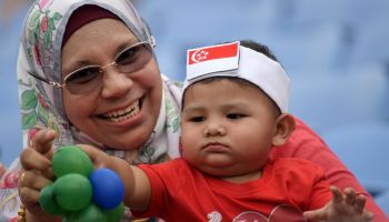 A woman holds a baby wearing a headband with the Singapore national flag as they wait for the start of the 54th National Day Parade in Singapore on August 9, 2019.