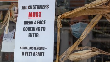 A worker places a placard on the window of a liquor store while wearing a face mask on April 10, 2020 in Jersey City, New Jersey.