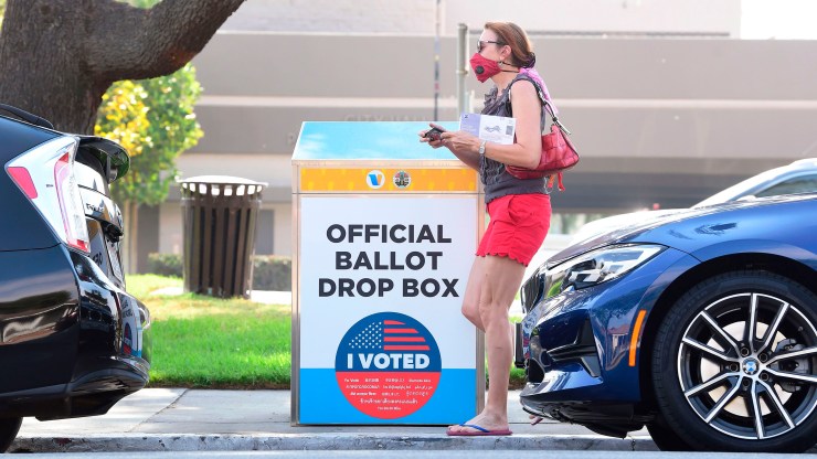 A woman holding her ballot walks past a Vote by Mail Drop Box for the 2020 US Elections on October 5, 2020 in Monterey Park, California, on the first day drop boxes are available to voters.