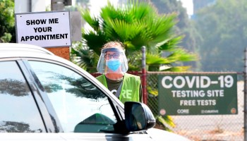 A volunteer wearing face mask and face shield checks for COVID-19 test appointments from motorists arriving at Dodger Stadium in Los Angeles, California on October 8, 2020.