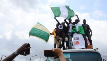 Youths of ENDSARS protesters display the Nigerian flag and a placard in a crowd in support of the ongoing protest against brutality of the Nigerian police force unit called Special Anti-Robbery Squad (SARS).