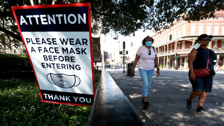 Visitors walk past face mask signs along Decatur Street in the French Quarter on July 14 in New Orleans.