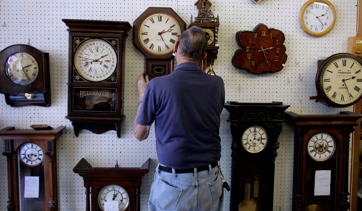 A man hangs a clock on a wall full of them.