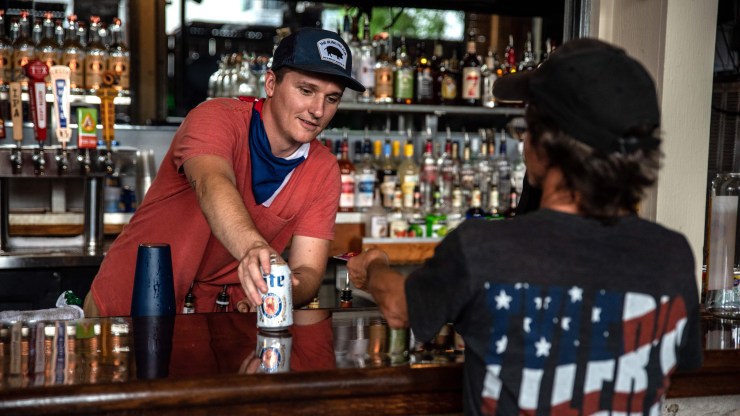 A bartender without a mask serves a beer to a customer, who is also not wearing a mask, at a bar in Austin, Texas, in May.