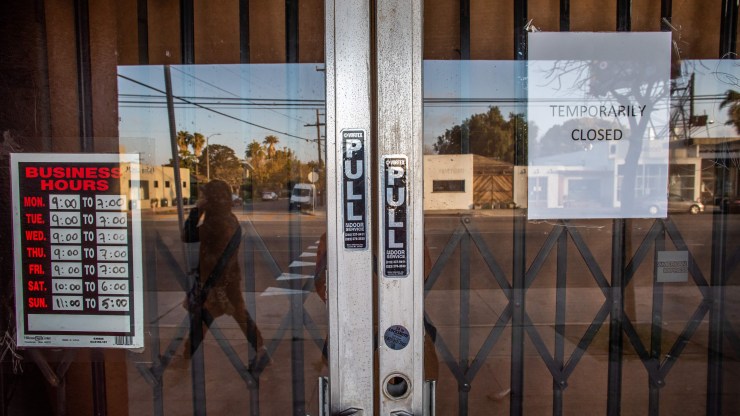 A person walks by a business with a "temporarily closed" sign on their door in Venice Beach, California.