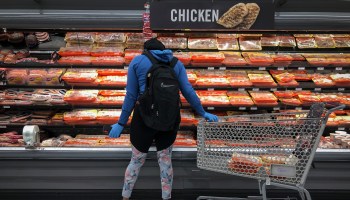 A woman wearing gloves is seen from behind shopping for chicken at a grocery store in Washington, D.C., in April.