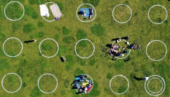 An aerial view of people sitting in socially distanced spray painted circles while picnicking at Mission Dolores Park in San Francisco, California.