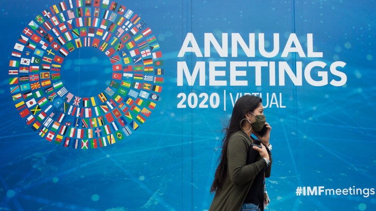 A woman walks past a promotional poster for the virtual 2020 Annual Meetings outside the International Monetary Fund at their headquarters in Washington, D.C., on Oct. 13, 2020.