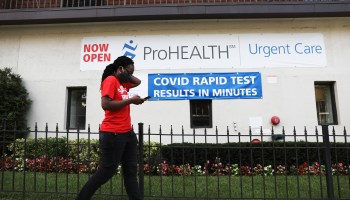 A man in a mask walks by a sign advertising new rapid COVID-19 tests with results in minutes on an urgent care health clinic in Brooklyn, New York.