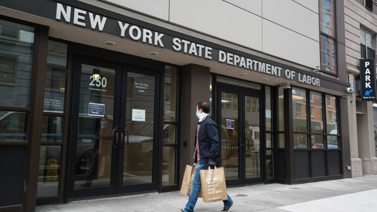 A man in a face mask walks past the New York State Department of Labor building in Brooklyn.