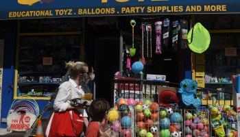 Two woman and a child wearing face masks walk past an open toy store in June in New York City.