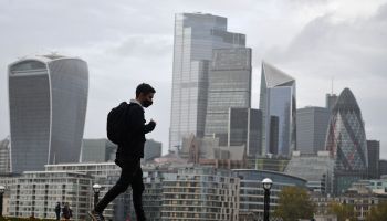 A man walks along the southern bank of the River Thames with the office towers of the City of London in the background in London on November 1, 2020.