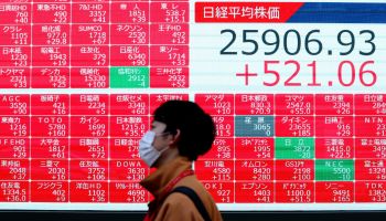 A man wearing a face mask walks past an electronic board showing share prices of the Tokyo Stock Exchange and closing numbers of Nikkei 225 index in Tokyo on November 16, 2020.