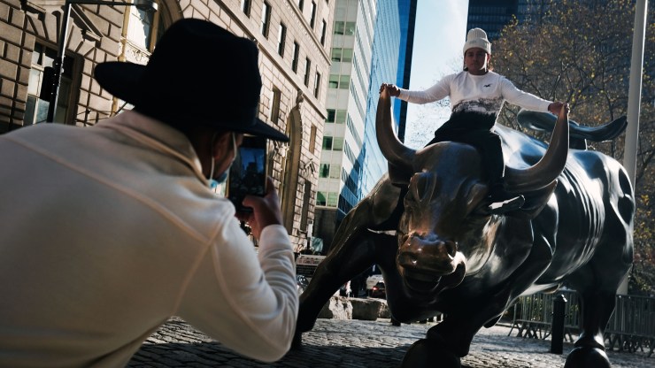 A man sits on the Wall Street bull near the New York Stock Exchange (NYSE) on November 24, 2020 in New York City. As investors' fear of an election crisis eases, the Dow Jones Industrial Average passed the 30,000 milestone for the first time on Tuesday morning.