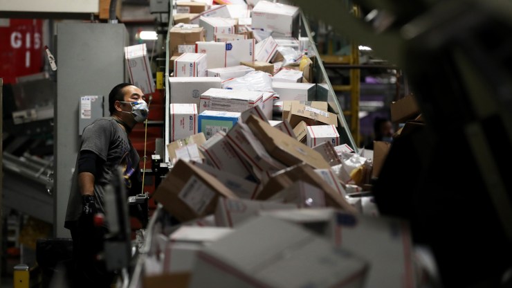 A postal worker wearing a mask monitors packages on a conveyor belt at a processing and distribution center on April 29, 2020, in Oakland, California.