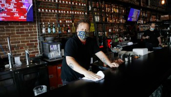 A bartender with a face mask wipes down the bar while awaiting patrons at a Florida restaurant. Anxiety is rising for many small business owners.