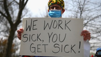 A health care worker holds a sign that reads "We work sick, you get sick" as nurse and health care workers rally against a paid sick leave policy in April in the Bronx, New York.