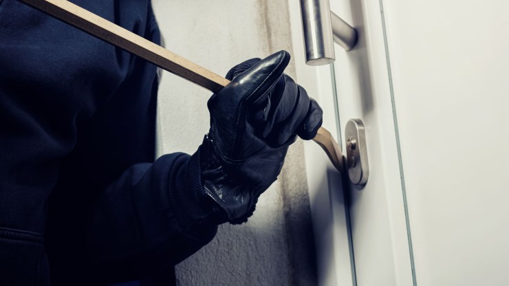 This stock image shows a burglar using a crowbar to break into a home at night.