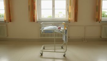 A 4-day-old newborn baby lies in a baby bed in the maternity ward of a hospital.