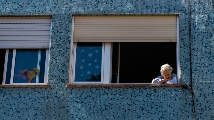 An elderly woman looks on from her window.
