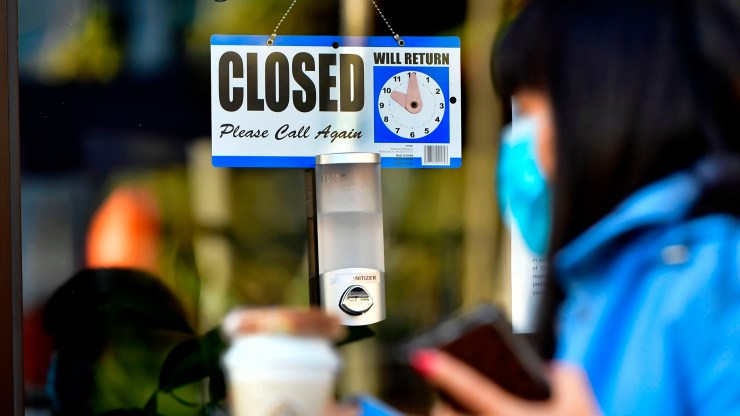 A pedestrian wearing her facemask and holding a cup of coffee walks past a closed sign hanging on the door of a small business in Los Angeles, California on November 30, 2020.