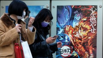 In this picture taken on December 16, 2020, pedestrians walk past a poster promoting the anime movie Demon Slayer -- Kimetsu no Yaiba the Movie: Mugen Train -- at a cinema in Tokyo. - An anime epic in which a teenager hunts down and beheads demons has become the surprise sensation of Japanese cinema during the pandemic, and could soon be the country's top-grossing film of all time. (Photo by Kazuhiro NOGI / AFP) / To go with AFP story Japan-entertainment-film-anime-health-virus, FOCUS by Mathias CENA, Katie Forster (Photo by KAZUHIRO NOGI/AFP via Getty Images)