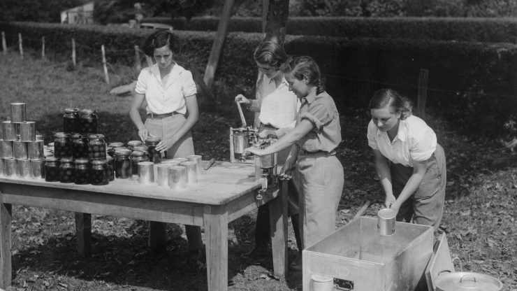 Black and white photo of girls canning and bottling plums in mason jars in 1944.