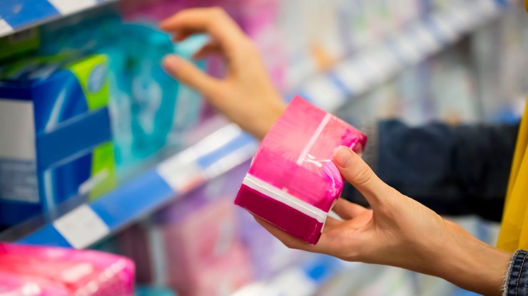 A woman looks at menstrual products in the aisle of a store.