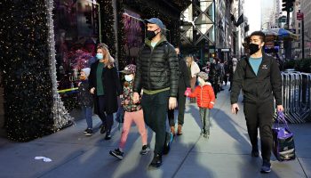 People wearing protective masks walk by holiday windows in New York City.