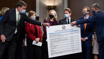 Sen. Joe Manchin, Democrat of West Virginia, hands a poster describing a proposal for a COVID-19 relief bill to Sen. Mark Warner, Democrat of Virginia, alongside a bipartisan group of Democrat and Republican members of Congress as they announce the proposal on Dec. 1, 2020.