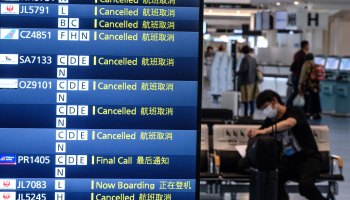 A traveler wearing a face mask sits past a departure board showing cancelled flights at Tokyo's Haneda Airport on March 10, 2020.