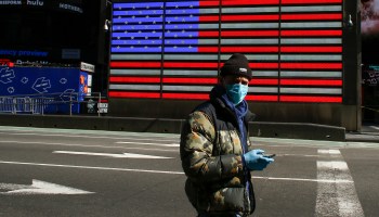 A man in a face mask passes an American flag in New York City. This year, the U.S. has added instability to the global economy, in contrast to its historical role of bolstering recovery.