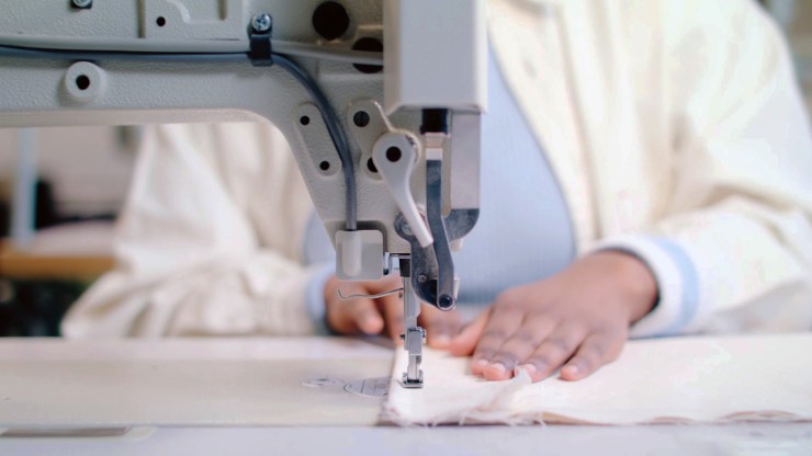 A closeup of a woman's hands pushing fabric through a sewing machine.