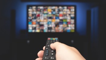 A picture of a person using a remote control while watching TV through a streaming service.