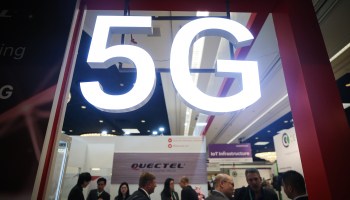 Attendees and workers chat beneath a 5G logo at the Quectel booth at CES 2020 at the Las Vegas Convention Center on Jan. 8, 2020.