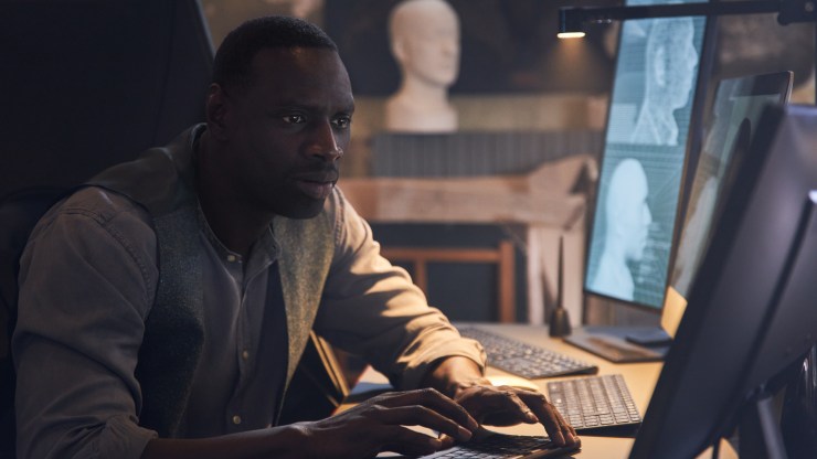 Omar Sy, who plays Assane Diop in "Lupin," studies a computer screen in this production still from the Netflix series.