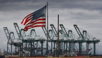 The U.S. flag flies over shipping cranes and containers in Long Beach, California on March 4, 2019.